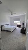 Neutral-toned wall-to-wall carpeting, ceiling fan with integrated lighting, and single-pane window with a roller shade