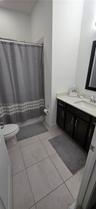 Bathroom featuring dark wood-finish cabinetry, a light-toned solid surface countertop, rectangular under-mount sink, tiled flooring, and a shower-tub 