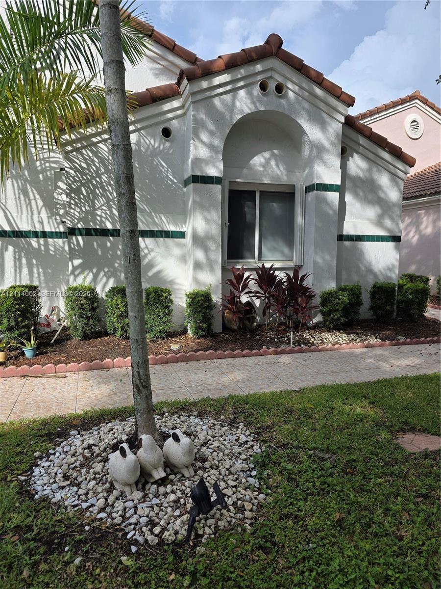 Stucco exterior featuring arched architectural detailing, decorative tile accents, and a tile roof, complemented by a paved walkway and mature landsca