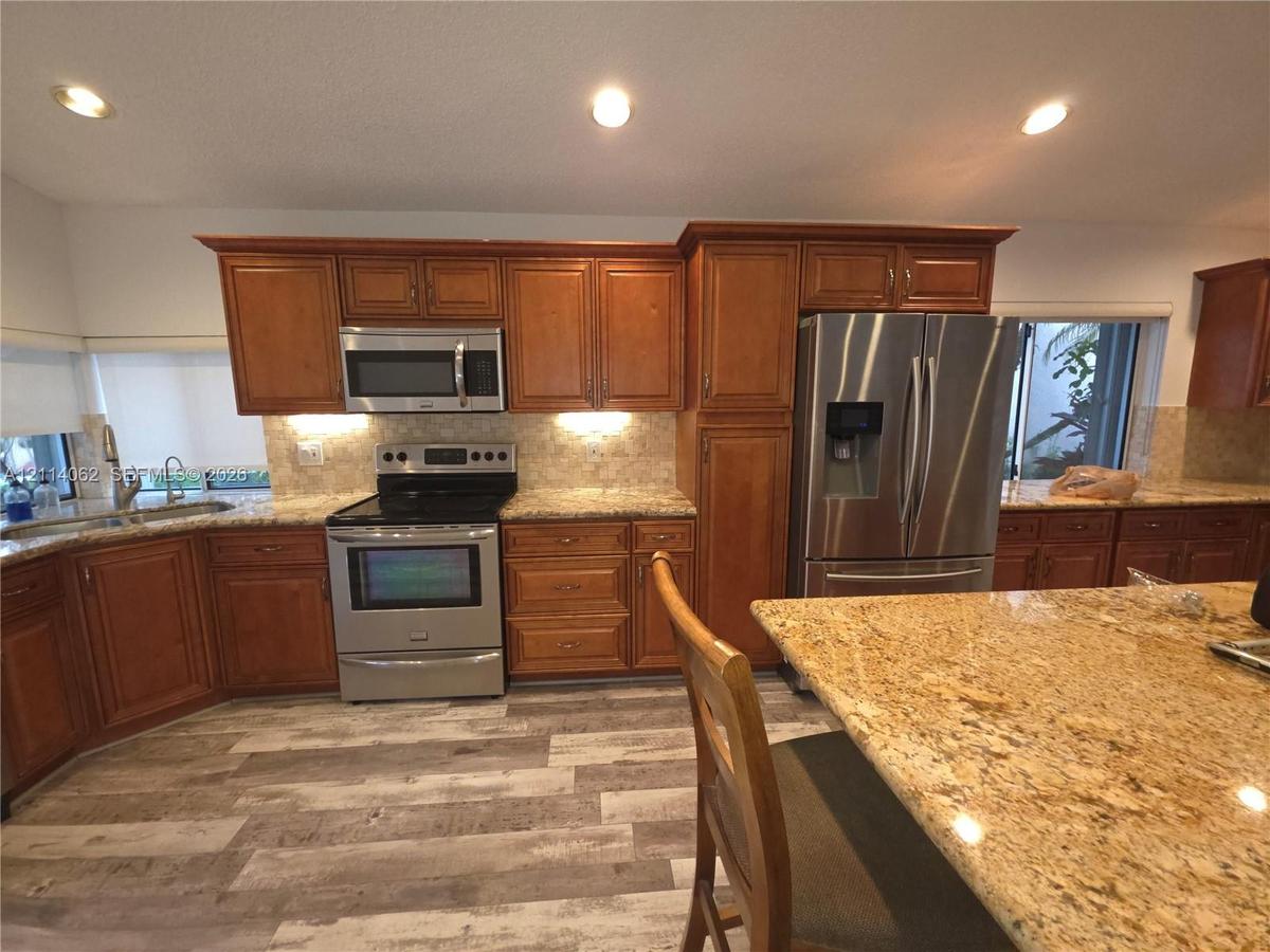Kitchen featuring wood cabinetry, stainless steel appliances, patterned stone countertops, wood-finish flooring, and recessed ceiling lighting