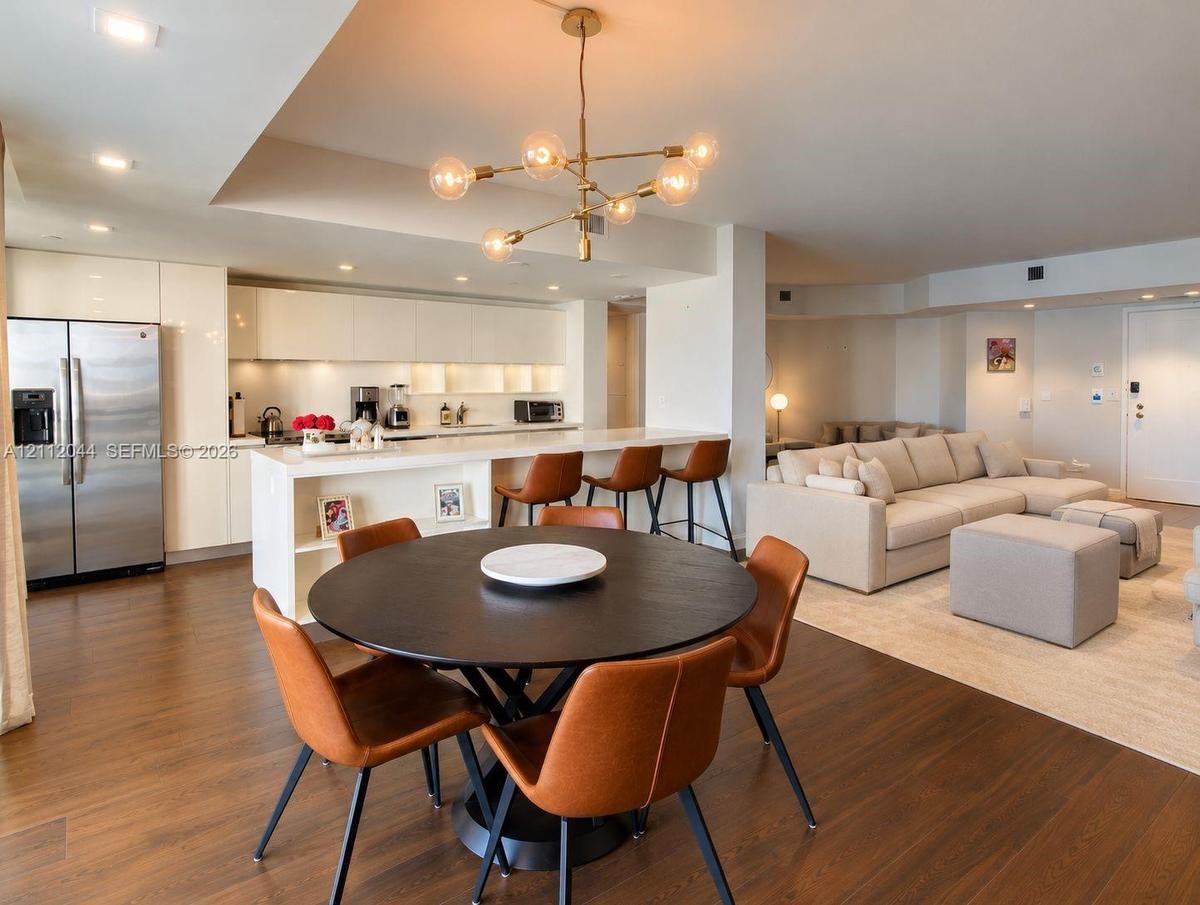 Open-concept kitchen featuring high-gloss cabinetry, stainless steel refrigerator, breakfast bar with waterfall-edge countertop, recessed lighting, an