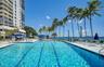 Resort-style swimming pool featuring lane markings, concrete decking, integrated lighting, and palm tree landscaping