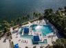 Waterfront pool complex featuring an expansive swimming area, integrated sun shelf, dual built-in shade structures, and surrounding paved decking