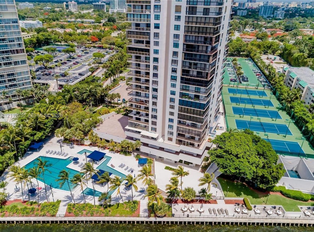 High-rise condominium tower featuring a resort-style swimming pool, multiple tennis courts, private marina access, and landscaped grounds