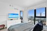 Floor-to-ceiling windows with expansive urban and water scenery, wood-finish flooring, and access to a private balcony