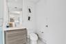 Bathroom featuring a floating wood-finish vanity, integrated white countertop with a recessed basin, chrome single-lever faucet, and large-format wall