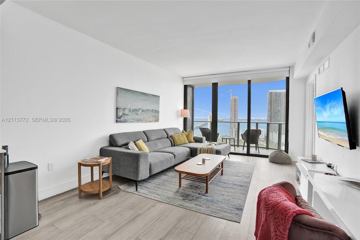 Living area featuring floor-to-ceiling windows, wood-finish flooring, and a private balcony with water and city skyline outlooks