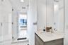 Bathroom featuring a wood-finish vanity with a light-toned countertop, integrated sink, chrome faucet, glass-enclosed shower, and full-height wall mir
