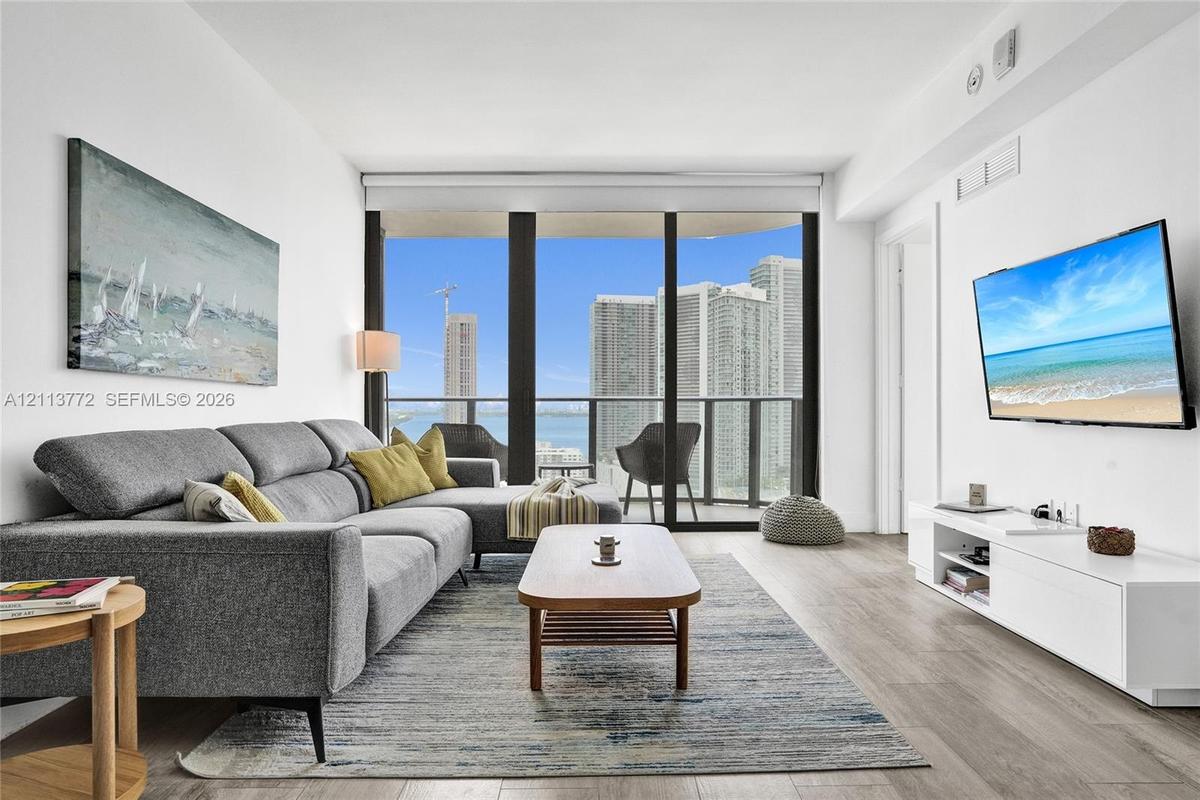Living area featuring wood-finish flooring, floor-to-ceiling windows, and a private balcony