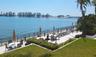 Waterfront patio featuring stone pavers, black metal perimeter fencing, manicured lawn, and mature landscaping
