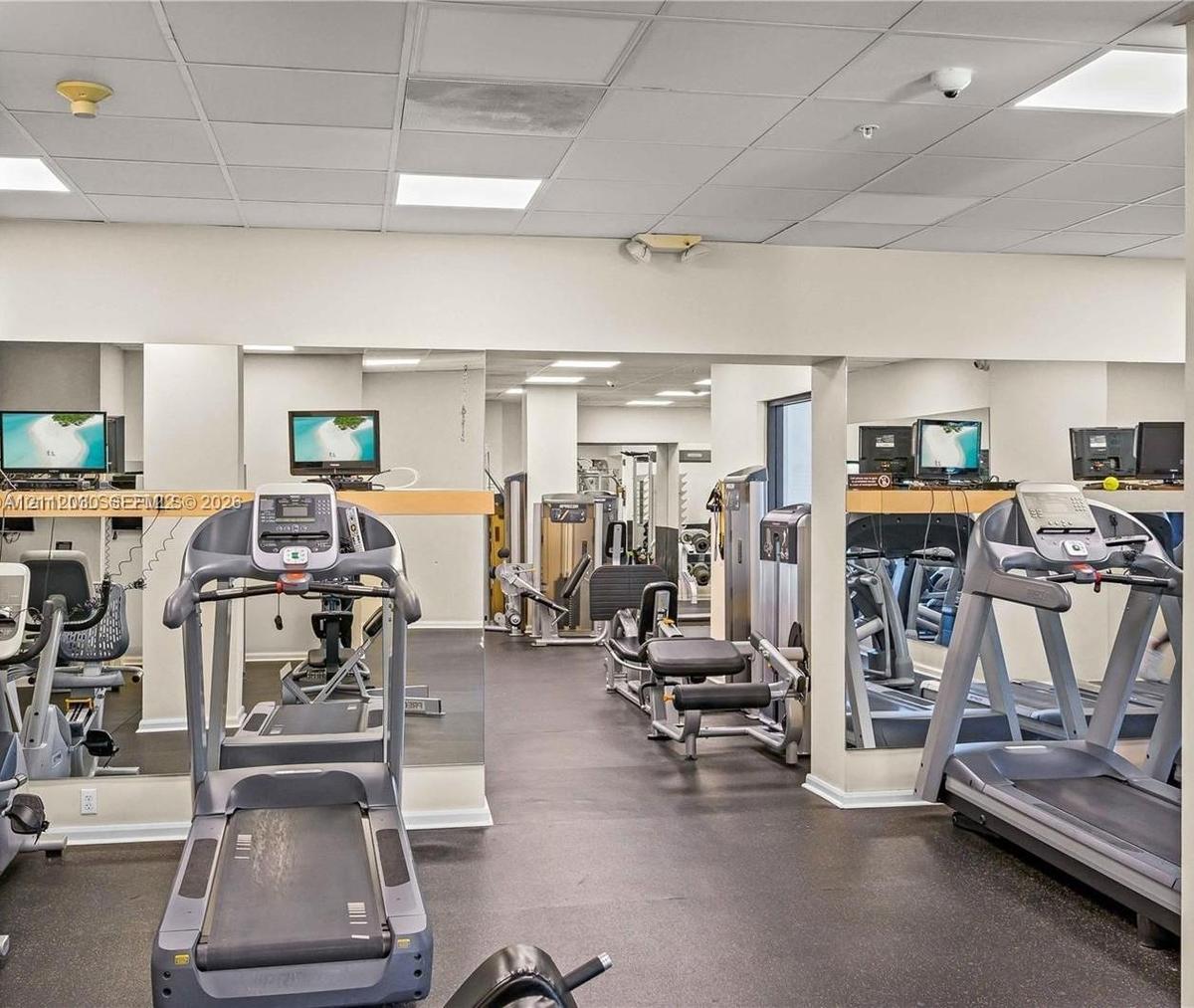 Fitness area featuring rubber flooring, expansive wall-to-wall mirrors, and recessed ceiling lighting