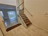 Staircase featuring wood-finish treads, glass panel railing with metallic standoffs, and a wall-mounted metal handrail, complemented by neutral tile f