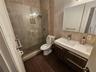 Walk-in shower with a glass enclosure, wall-mounted showerhead, and a recessed tiled niche, featuring a wood-finish floating vanity with a dual-basin 