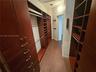Custom walk-in closet featuring extensive dark wood-finish cabinetry, built-in shelving, integrated hanging rods, and wood-finish flooring
