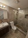 Walk-in shower with a glass enclosure, integrated tile niche, and pebble-style floor tiling, complemented by wood-finish cabinetry, a rectangular vess