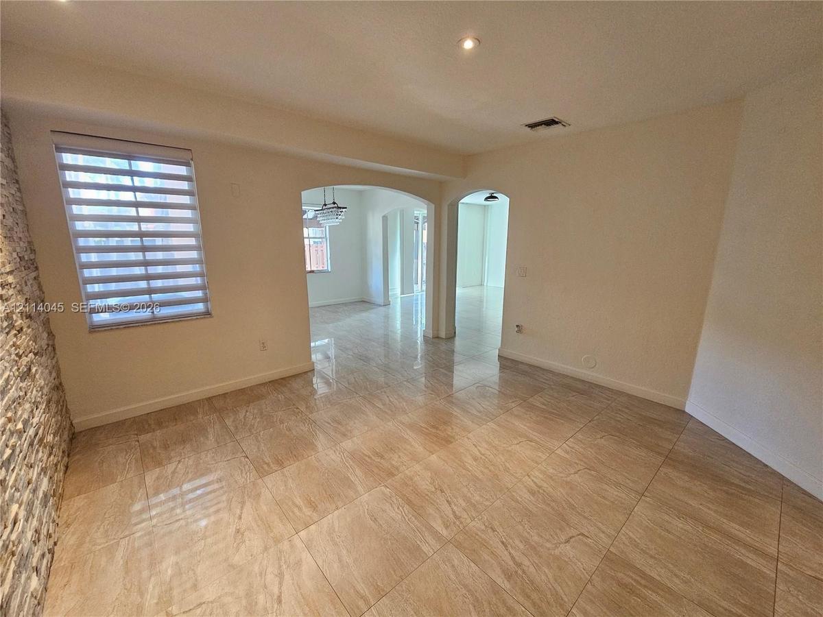 Interior space featuring large-format tile flooring, stacked stone wall accent, arched architectural openings, recessed lighting, and multi-layered wi