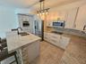 Kitchen featuring shaker-style cabinetry, stone countertops, stainless steel appliances, stone-accented center island with an undermount sink, and til