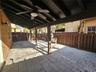 Covered patio featuring concrete paver flooring, dark-stained wood support beams, built-in ceiling fans, an exterior wall-mounted light fixture, and a