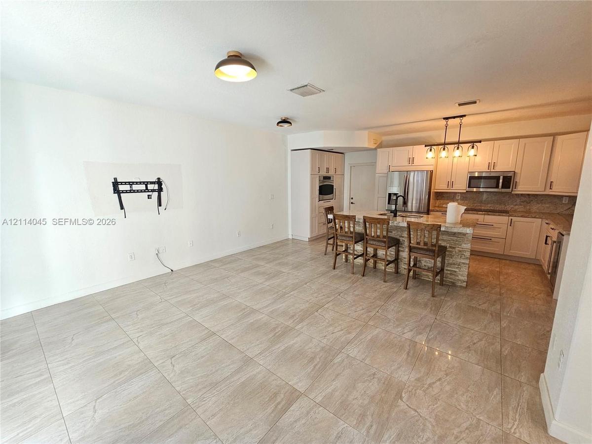 Kitchen featuring shaker-style cabinetry, stone-finish countertops, stainless steel appliances, a multi-pendant lighting fixture, and tile flooring