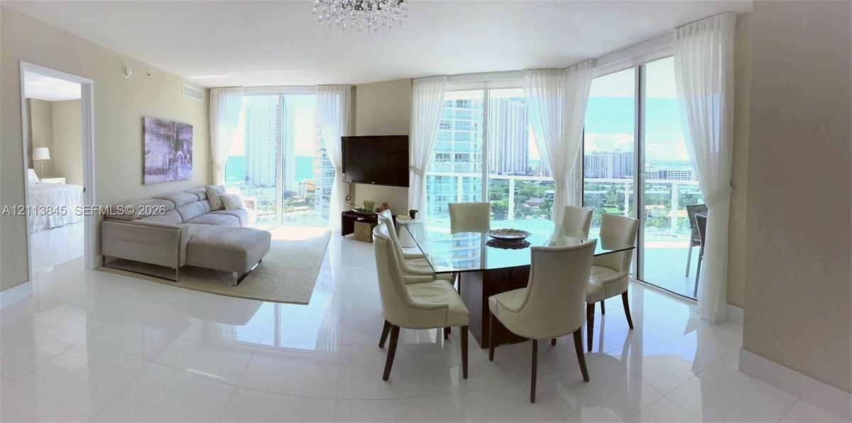 Open-concept living and dining area featuring polished tile flooring, floor-to-ceiling glass sliding doors, and a crystal chandelier