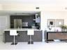 Kitchen featuring flat-panel dark wood cabinetry, a breakfast bar with stone-surface countertop, stainless steel appliances, and high-gloss flooring