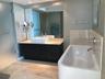 Dark wood-finish vanity with a rectangular vessel sink and countertop, large wall-mounted mirror, soaking tub with polished chrome fixtures, and large