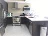 Kitchen featuring dark-finish cabinetry, stainless steel appliances, a chimney-style range hood, solid-surface countertops, and large-format tile floo