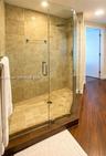Walk-in shower featuring a frameless glass enclosure, neutral stone tile surround, integrated shower bench, square rainfall showerhead, and wood-finis