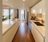 Modern kitchen featuring high-gloss cabinetry, expansive solid-surface countertops, wood-finish flooring, recessed lighting, and stainless steel appli