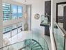 Double-height living area featuring floor-to-ceiling windows, polished stone flooring, custom glass-panel staircase with metal railing, and contempora