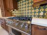 Stainless steel gas range with a heavy-duty burner grate, decorative multi-colored tile backsplash, solid-surface countertops, and wood-finish cabinet