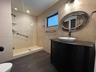 Bathroom featuring wood-finish flooring, textured stone-style wall tile, a glass-enclosed walk-in shower with integrated shelving, and a dark-toned va