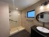Walk-in shower with a glass enclosure, textured stone-tile wall, wood-finish flooring, oval vanity mirror, and vessel sink with an oil-rubbed bronze f