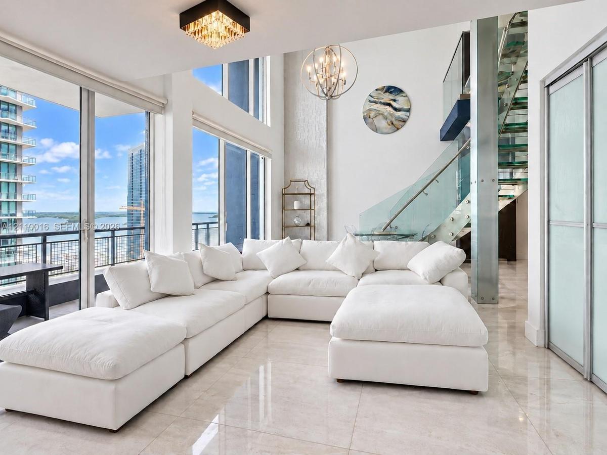 Kitchen featuring white cabinetry, stainless steel appliances, and large-format tile flooring, complemented by a curved staircase with glass treads an