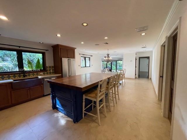 Kitchen featuring an expansive center island with a wood countertop, custom cabinetry, farmhouse sink, stone-finish tile flooring, and recessed lighti