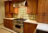 Custom stained-wood cabinetry, stainless steel professional-grade range, stainless steel range hood, patterned tile backsplash, and solid-surface coun