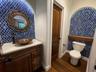 Custom vanity with stone countertop and copper vessel sink, arched alcoves with blue patterned tile work, wood-finish flooring, and solid wood interio