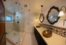 Double vanity featuring dual hammered metal vessel sinks, patterned tile backsplash, glass-enclosed walk-in shower with stone-finish surround, and dec