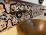 Hammered copper vessel sink paired with a wall-mounted bronze faucet and intricate patterned tile backsplash