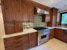 Custom wood cabinetry, stainless steel professional-grade gas range, stainless steel vent hood, patterned tile backsplash, and light-toned solid surfa