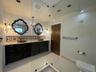 Dark wood dual vanity with light stone countertop, patterned ceramic tile backsplash, two decorative wall mirrors, and glass-enclosed shower