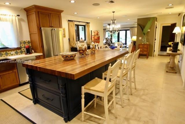 Kitchen featuring a large central island with a wood countertop, dark-finished cabinetry, stainless steel refrigerator, patterned tile backsplash, and