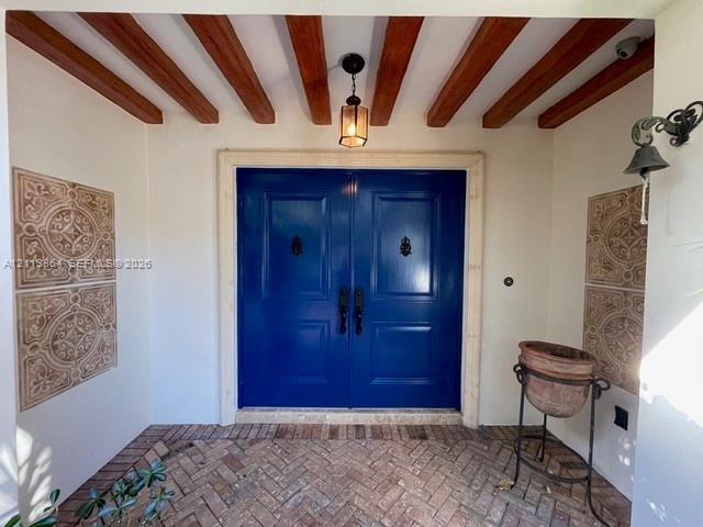 Entryway featuring double solid-panel doors with iron knockers, exposed wood ceiling beams, decorative wall tile accents, and herringbone-patterned br
