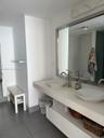 Dual-sink floating vanity with stone-surfaced countertop, white vessel sinks, tall-neck brushed metal faucets, and a full-width framed mirror