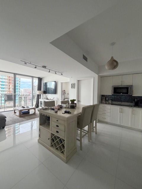 Open-concept living space featuring high-gloss tile flooring, floor-to-ceiling glass panel doors, a kitchen island with built-in wine storage, recesse