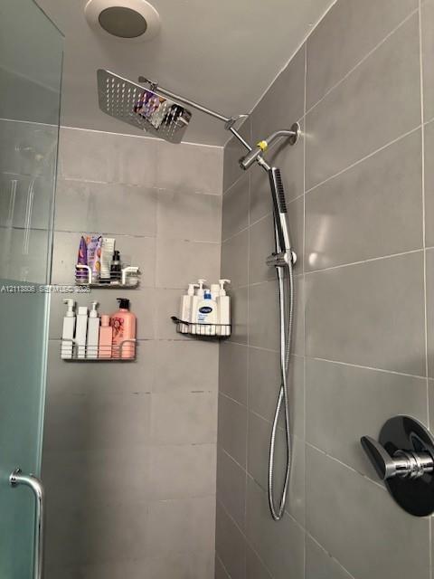 Shower enclosure featuring large-format grey wall tiling, a rainfall showerhead, a detachable hand-held sprayer, and a single-handle temperature contr