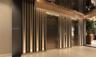 Floor-to-ceiling slatted wall paneling with integrated vertical accent lighting, metallic elevator doors, and neutral wide-plank flooring