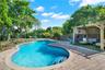 Freeform swimming pool with paver stone decking and attached wooden pergola featuring a lattice privacy screen