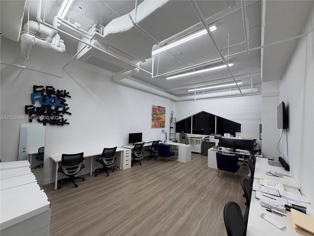 Industrial-style workspace featuring high exposed ceilings with linear lighting, wood-finish flooring, and a large custom-shaped window