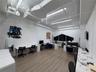Industrial-style workspace featuring high exposed ceilings with linear lighting, wood-finish flooring, and a large custom-shaped window